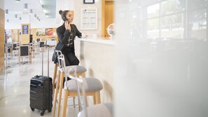 A person sitting at a bar with a suitcase and a laptop, in a well-lit indoor space with tables and chairs.