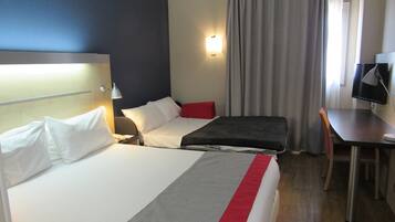 Ett hotellrum med två sängar, ett skrivbord, en stol, en TV och ett fönster med gardiner.