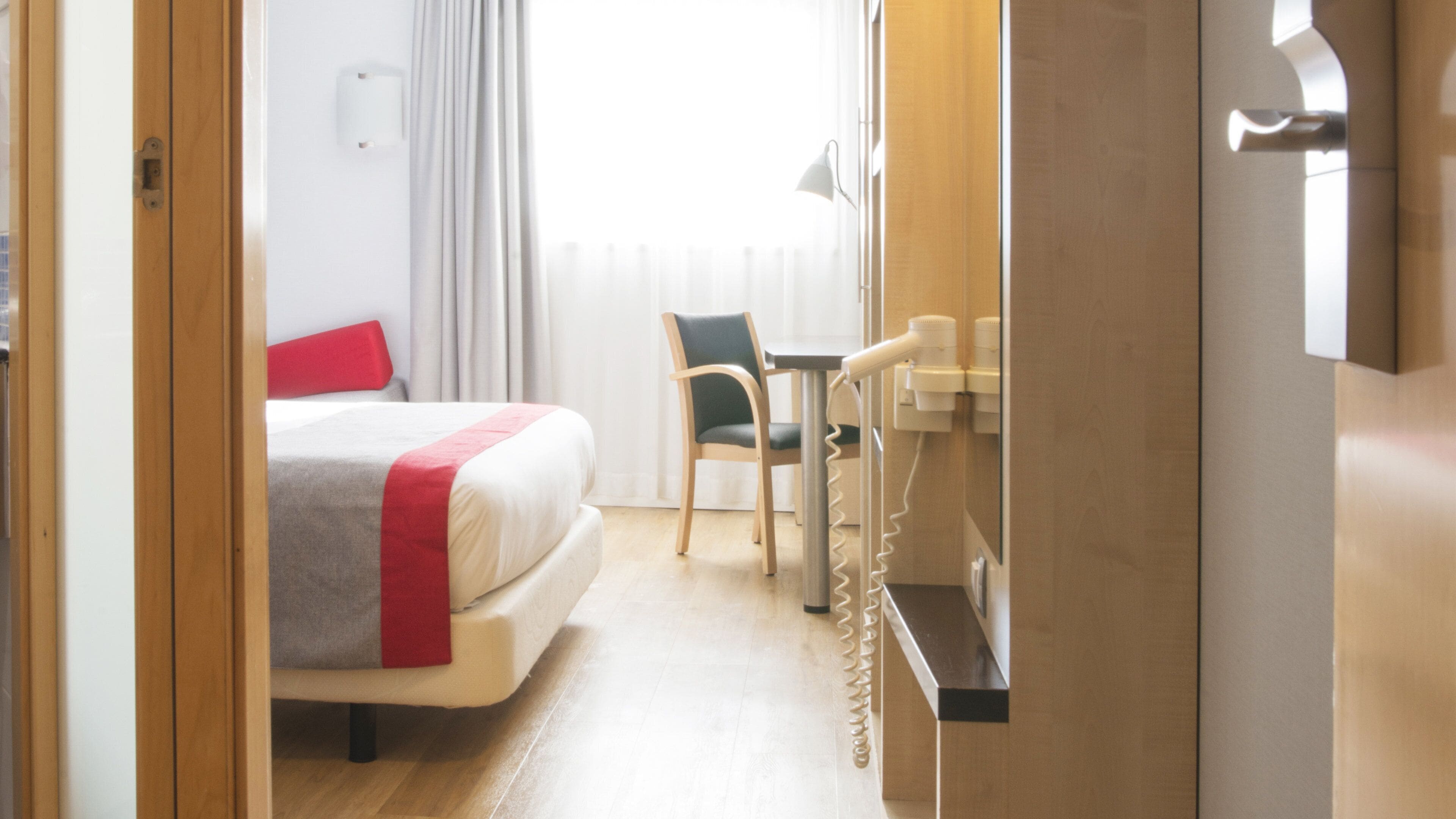 A hotel room with a bed, a chair, a desk with a telephone, and a mirror.