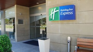 A Holiday Inn Express sign on a building facade with a glass entrance and a planter with green foliage. - Holiday Inn Express Valencia - Bonaire by IHG (Quart de Poblet)