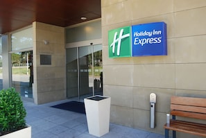 A Holiday Inn Express sign on a building facade with a glass entrance and a planter with green foliage.