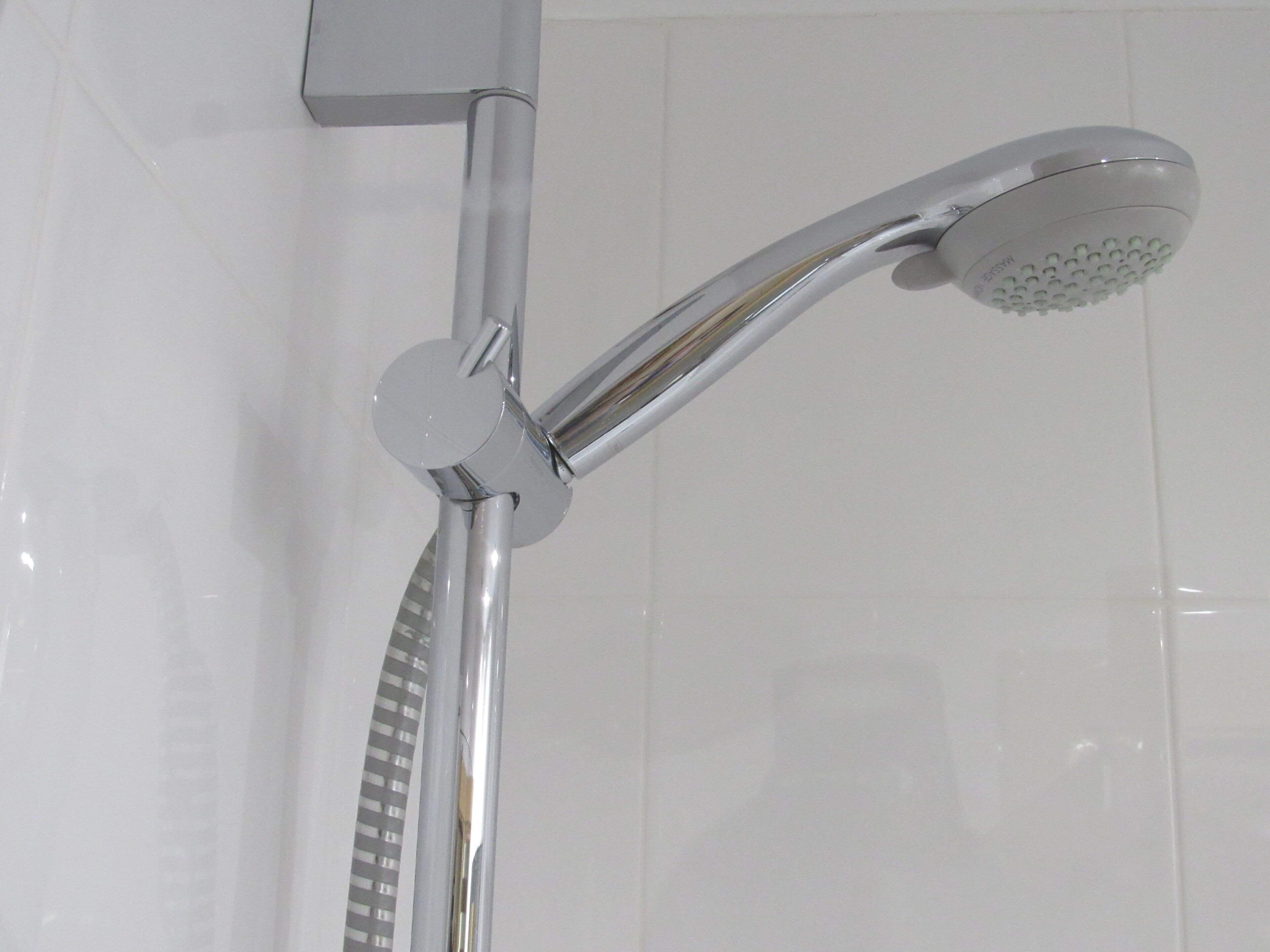 A chrome showerhead with a handheld attachment, mounted on a wall with a white tiled surface.