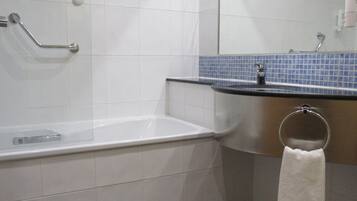 A bathroom with a white bathtub, a sink with a blue tiled backsplash, and a towel hanging on a metal ring.