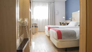 Habitación de hotel con dos camas, un escritorio, una silla, un teléfono y una ventana con cortinas.