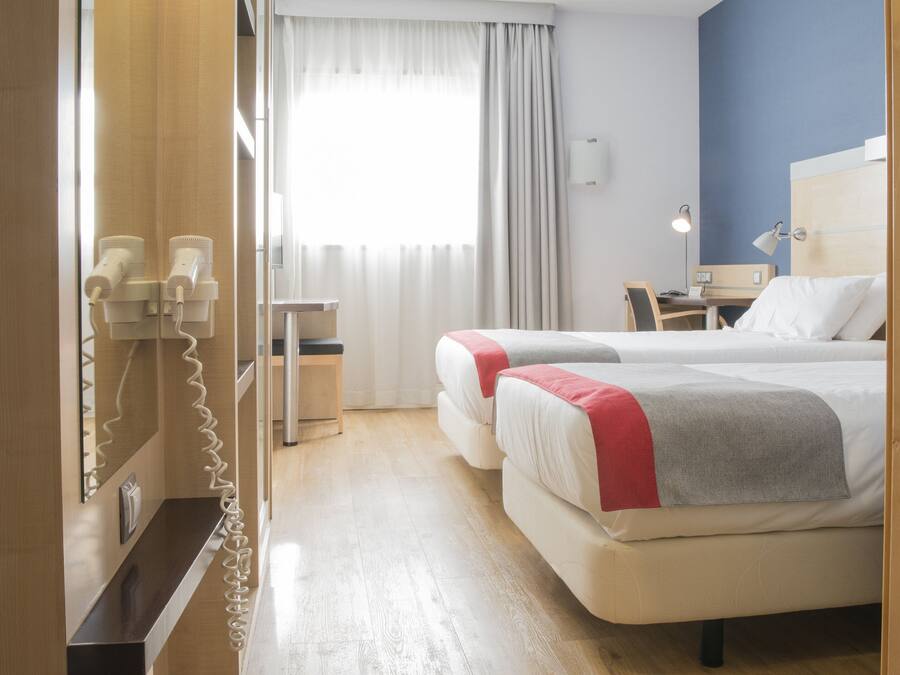 Habitación de hotel con dos camas, un escritorio, una silla, un teléfono y una ventana con cortinas.