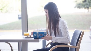 Una persona sentada a una mesa con un libro, un vaso de jugo de naranja y un plato de comida.