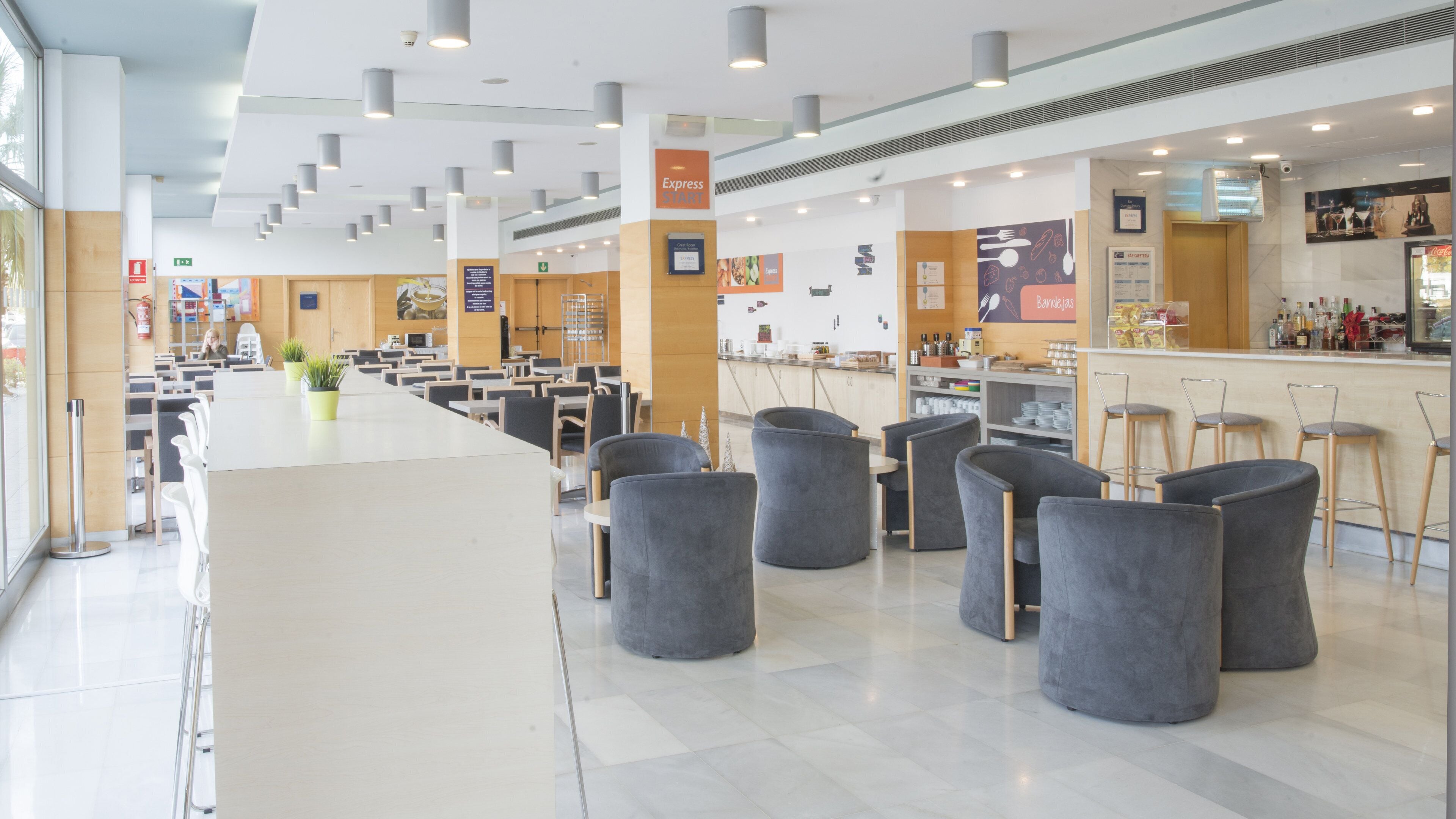 Een ruime cafetaria met hoge plafonds, moderne verlichting en een centraal bedieningsgedeelte.