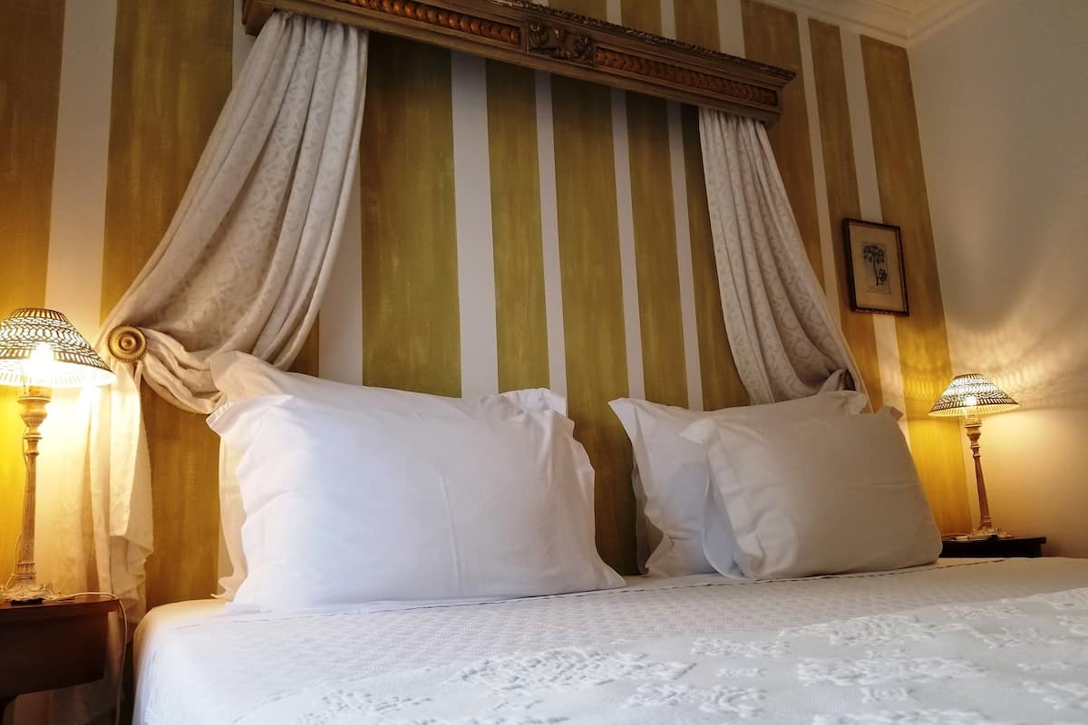Une chambre d’hôtel avec un lit, deux lampes de chevet, un lit à baldaquin et un tableau au mur.