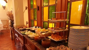 A buffet with various food items, including pastries, bread, and condiments, arranged on a counter with a tiled floor and wooden cabinets.