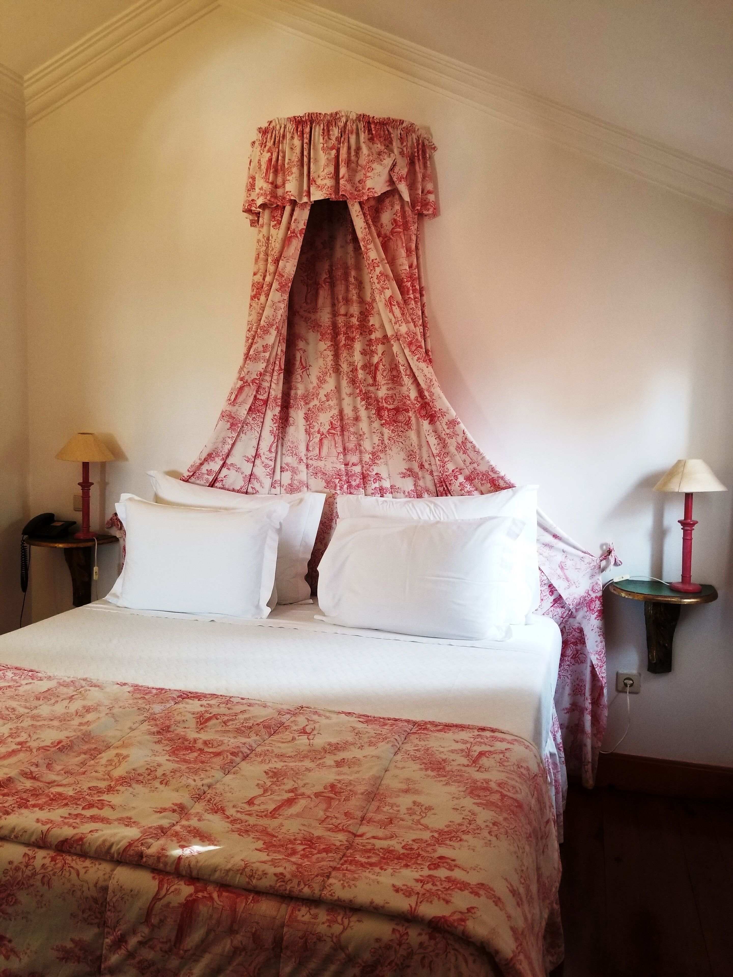 Un letto a baldacchino, due comodini con lampade e un telefono fissato al muro.