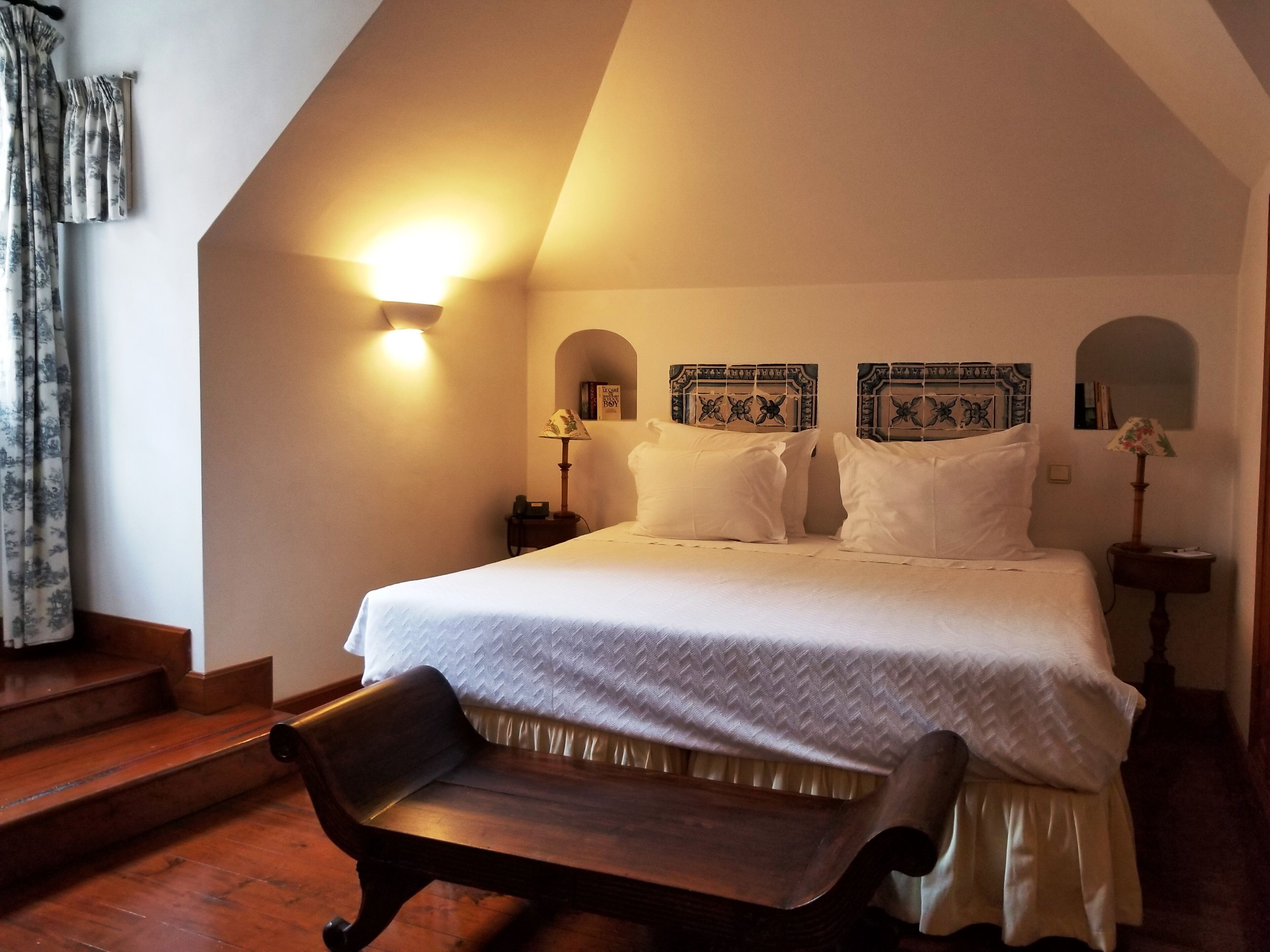 Una camera da letto con un letto grande, due comodini, una panca e una scala.