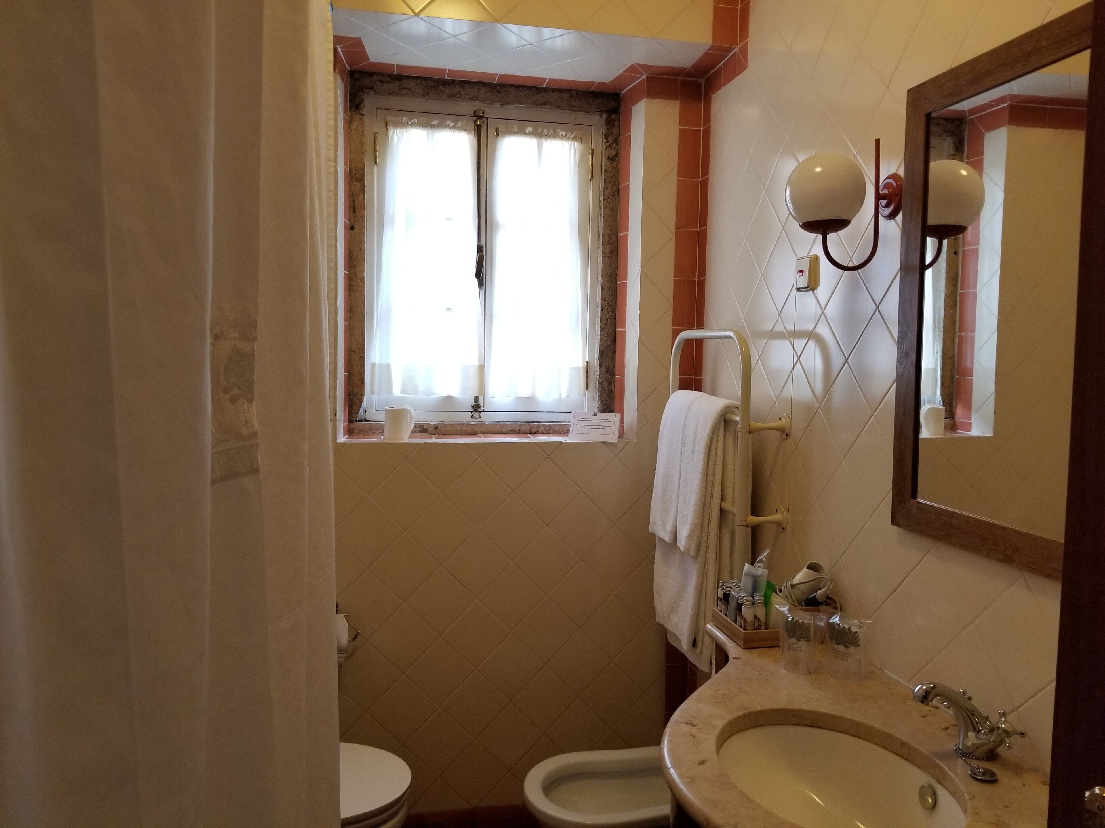 Un baño con inodoro, lavamanos y ventana con cortinas.