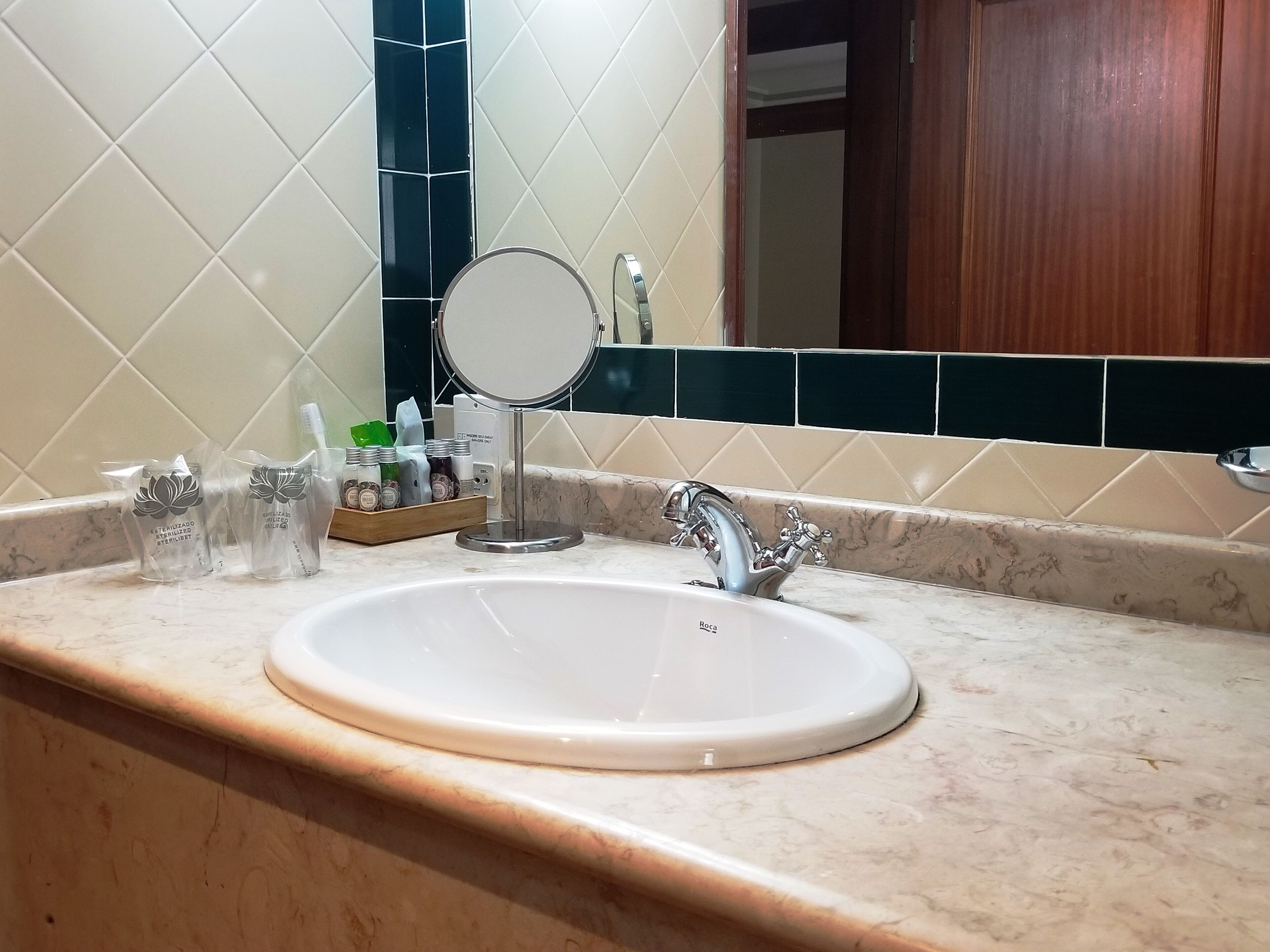 Ein Badezimmer mit einem weißen Waschbecken, einem Spiegel und Toilettenartikeln auf der Ablagefläche.