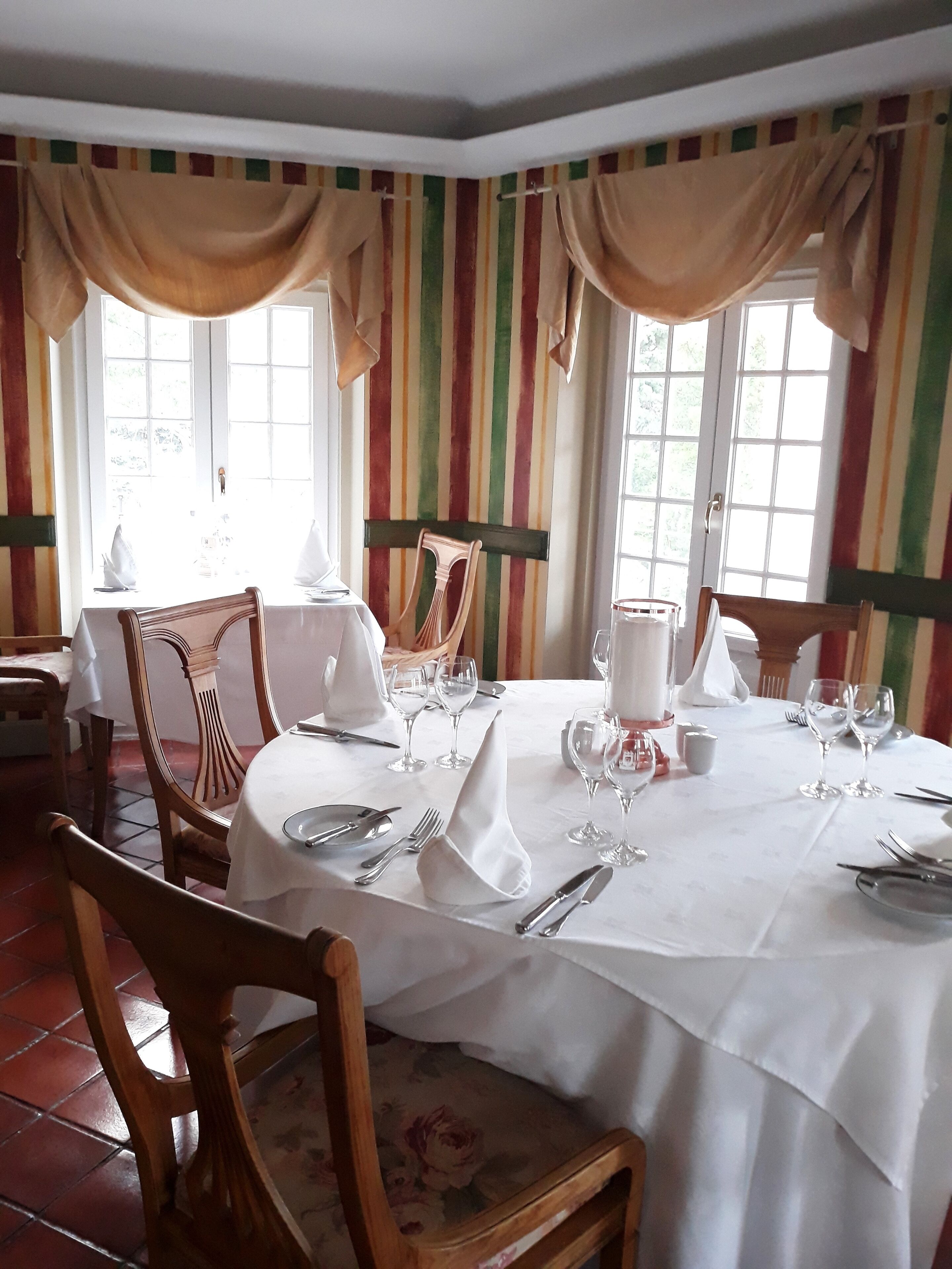 Une salle à manger avec une table ronde dressée pour quatre personnes, des chaises et une fenêtre avec des rideaux.
