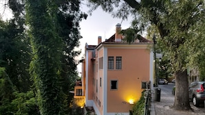 A two-story building with a light orange facade, surrounded by dense greenery.