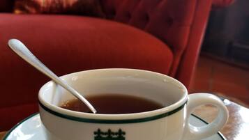 Una taza de té sobre un platito con una cuchara, sobre una mesa en una habitación con un sofá rojo y un cojín al fondo.