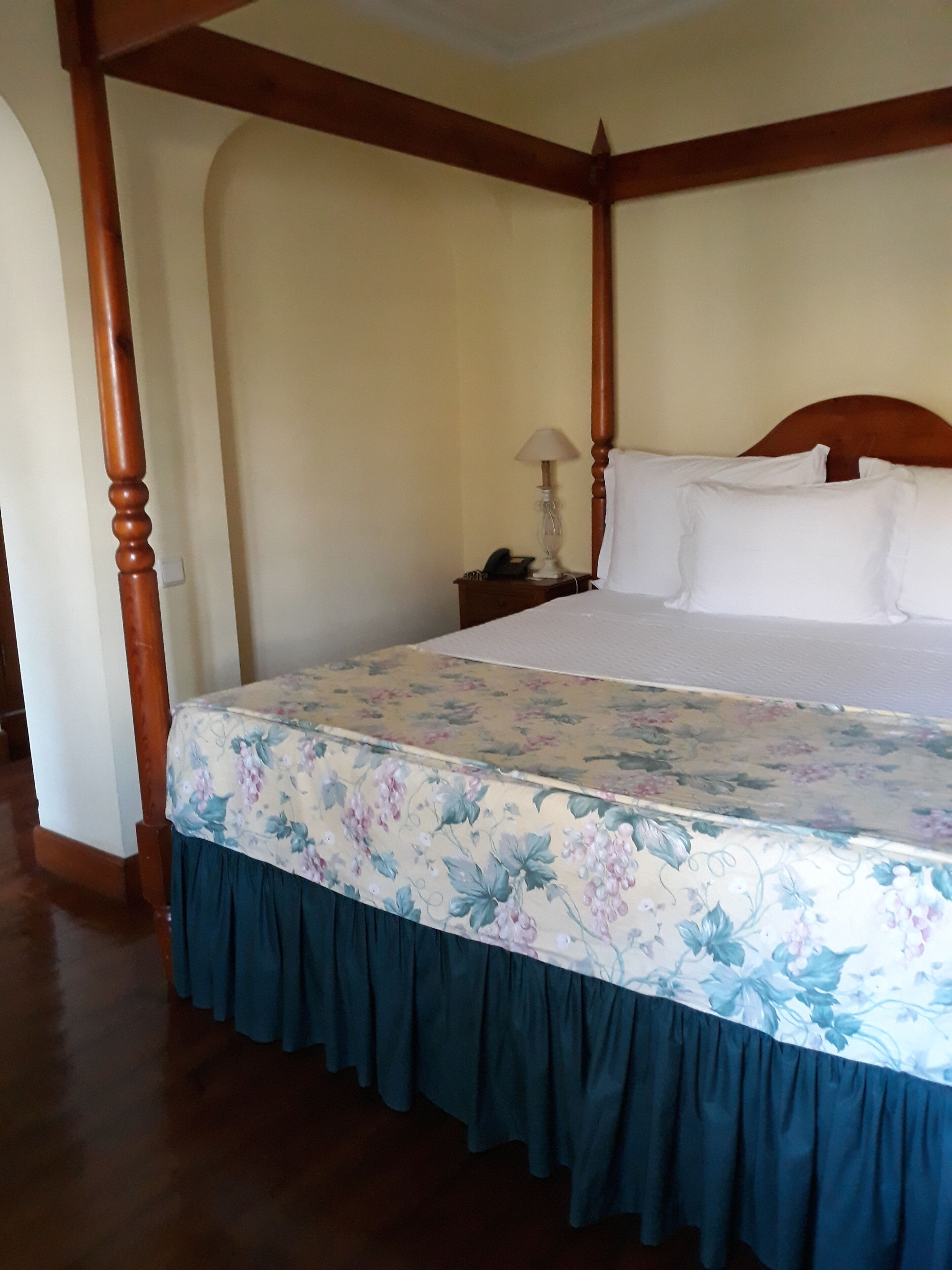 A four-poster bed with a floral bedspread and a dark blue skirt.