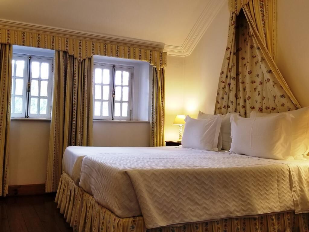 A hotel room with a bed, curtains, a window, and a lamp.