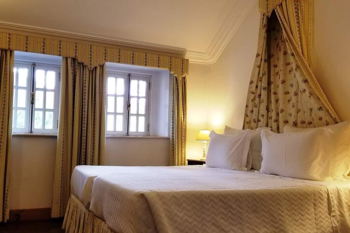 A hotel room with a bed, curtains, a window, and a lamp.