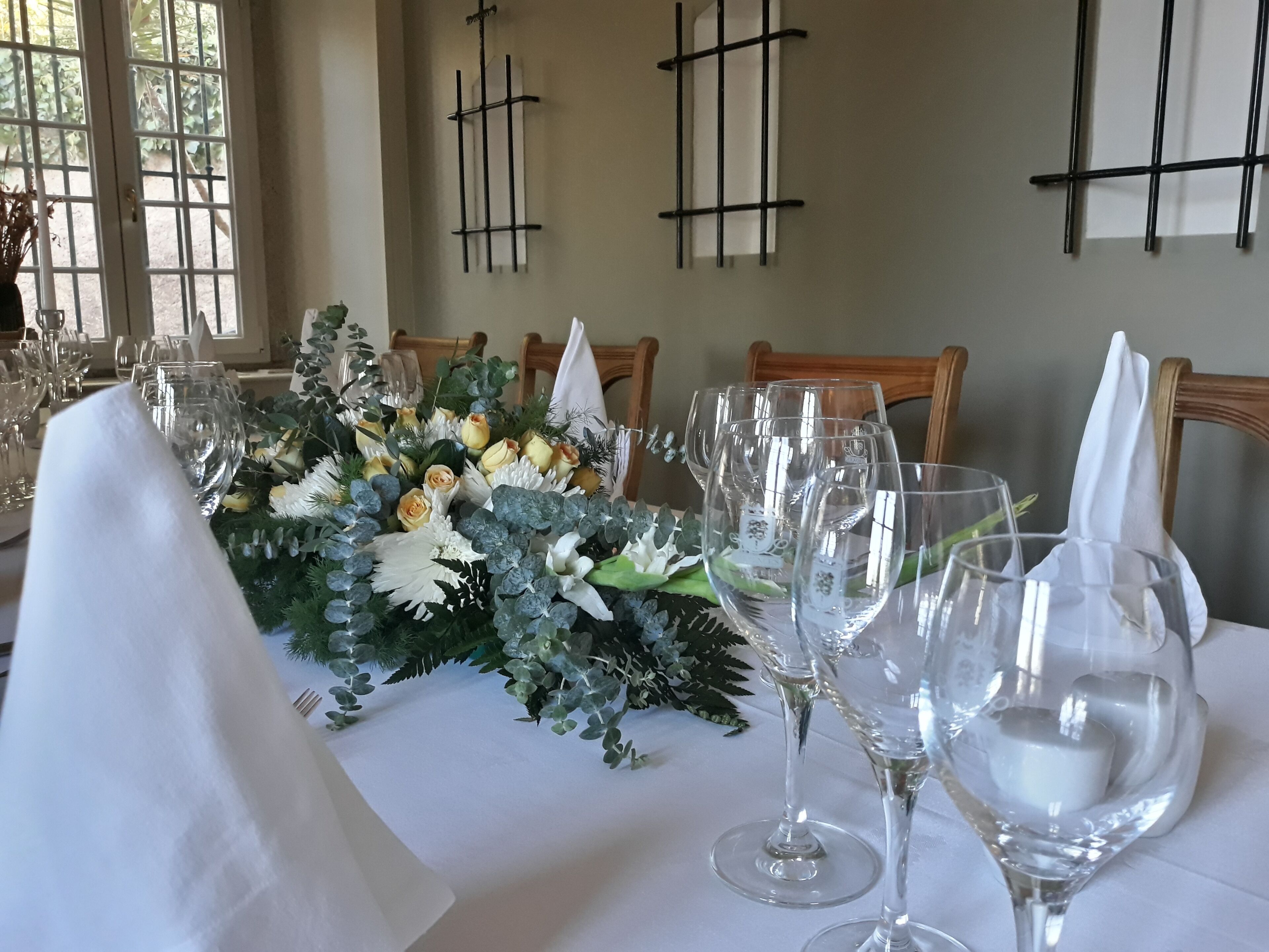 Ett matbord dukat med en vit duk, glas och en blomsterdekoration i mitten.