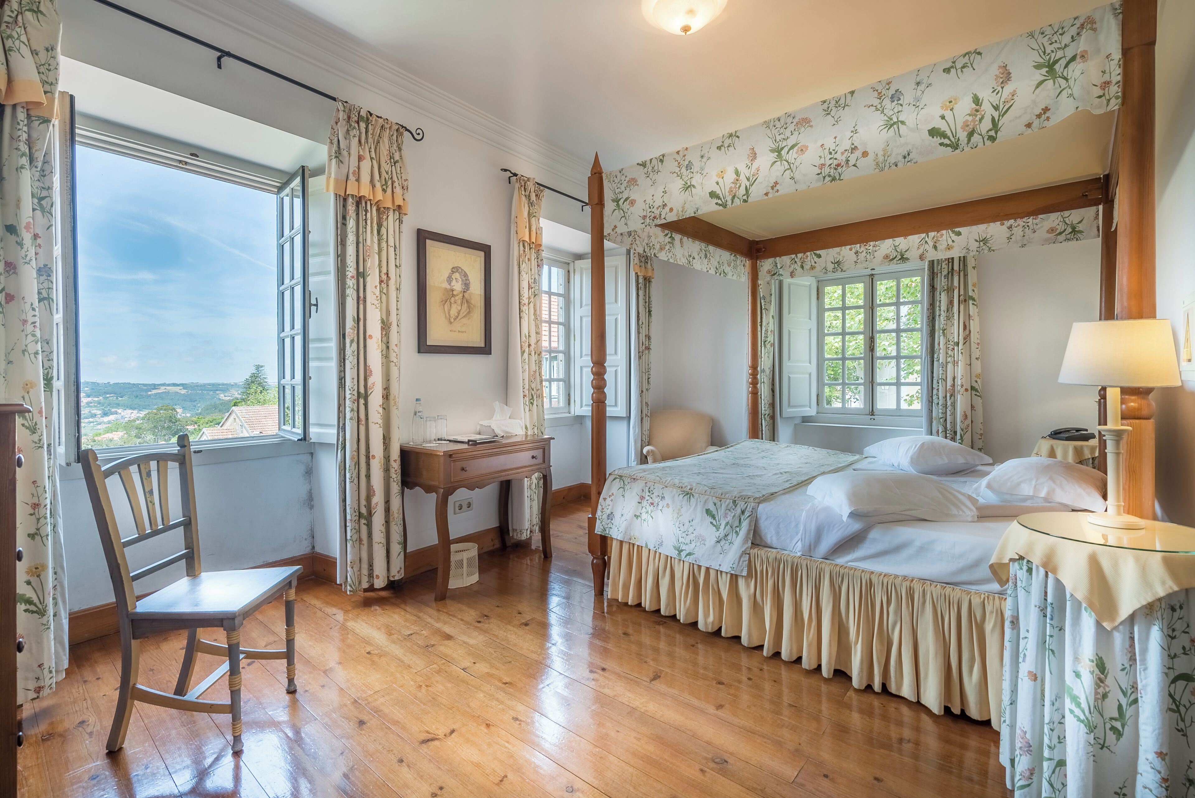 A bedroom with a four-poster bed, a wooden chair, a desk, and a window with curtains.