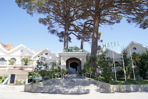 A hotel entrance with a staircase leading up to the main building, surrounded by trees and a clear sky.