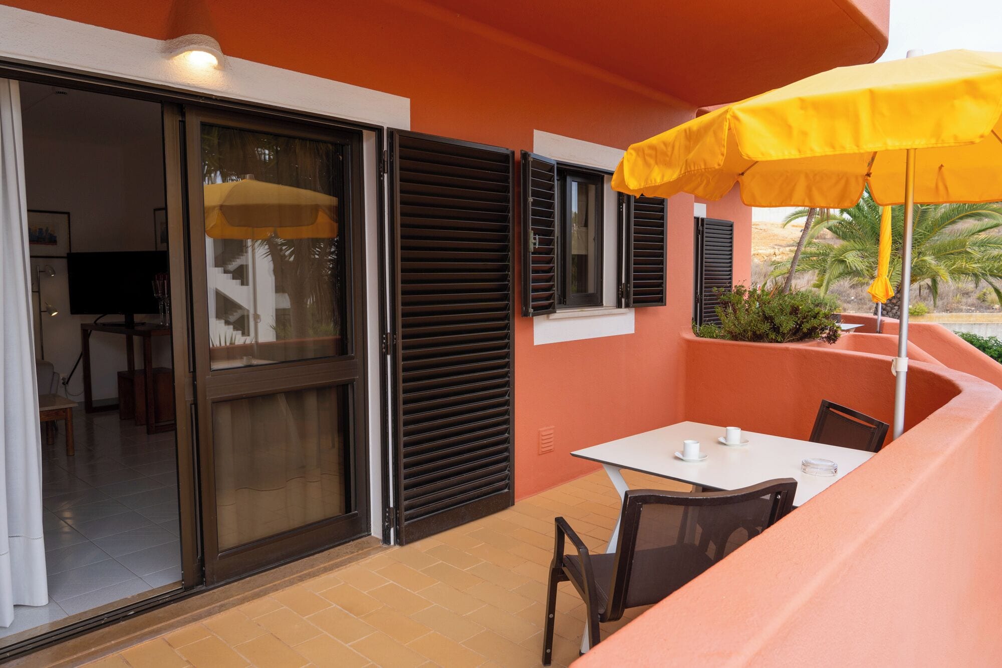 Eine Terrass mit Tisch und Stühlen, einem gelben Sonnenschirm und einer Glasschiebetür zu einem Innenraum.