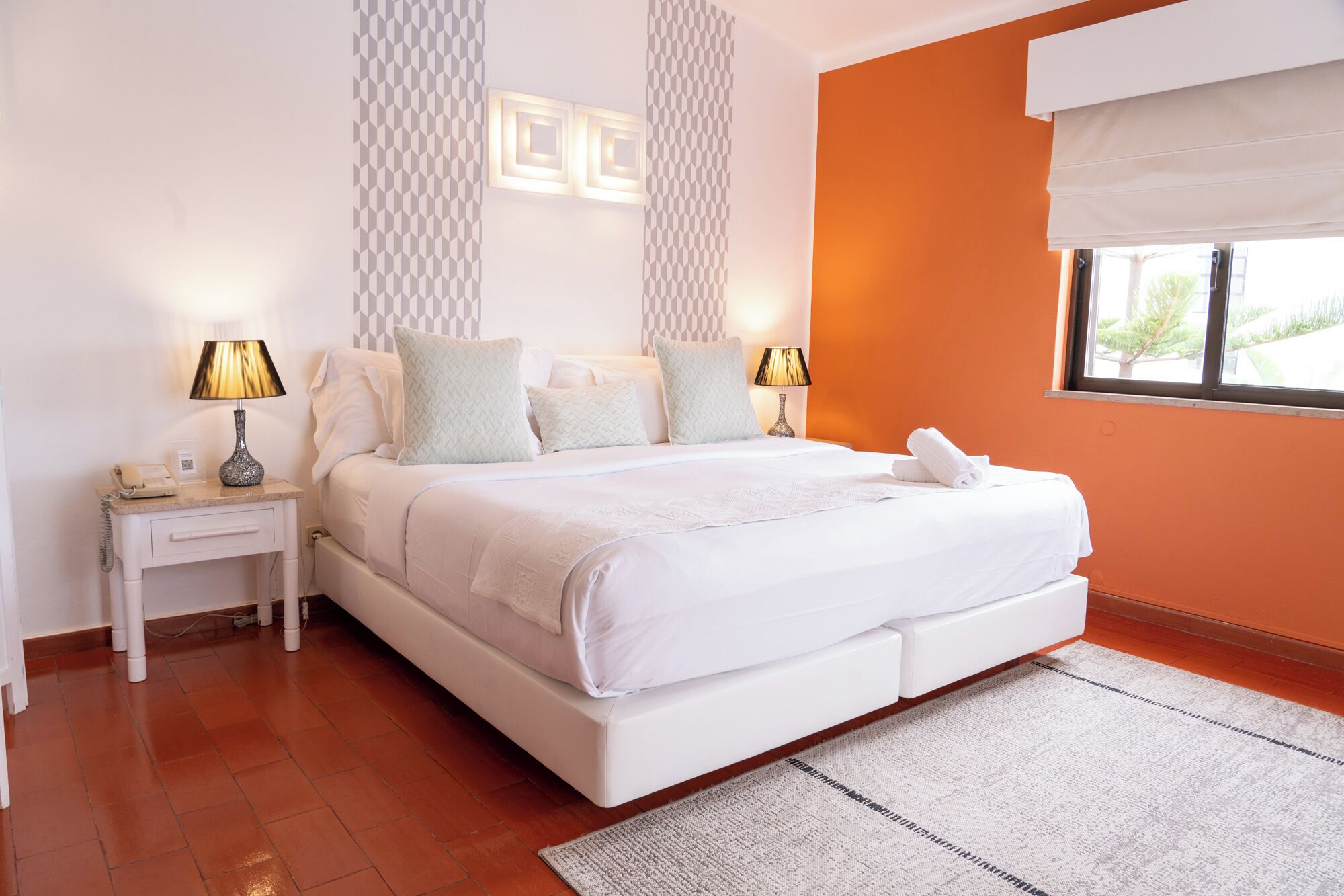 A modern bedroom with a large bed, two bedside tables, a nightstand, and a window with a view.
