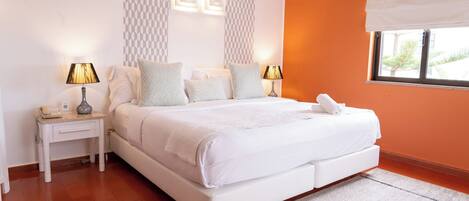 A modern bedroom with a large bed, two bedside tables, a nightstand, and a window with a view.