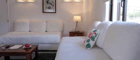 Une chambre d’hôtel avec deux lits blancs, une petite table avec une télécommande, une lampe et un tableau encadré au mur.