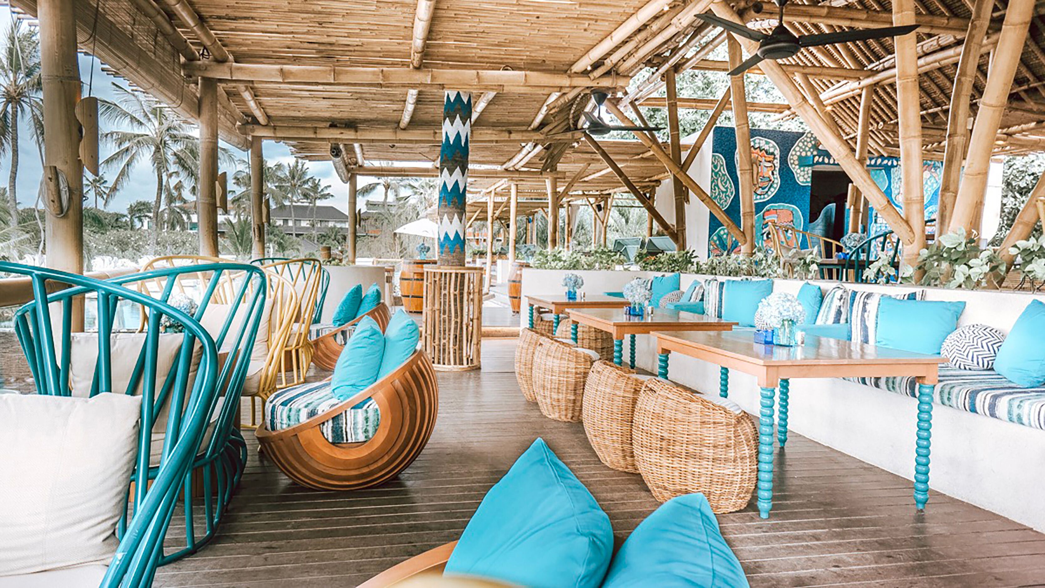 An outdoor seating area with wicker furniture and blue cushions, bamboo ceiling, and tropical plants.