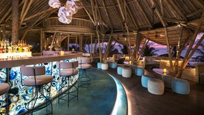 An indoor bar area with a thatched roof, bar stools, and a view of the sunset. - Bali Mandira Beach Resort & Spa (Legian)