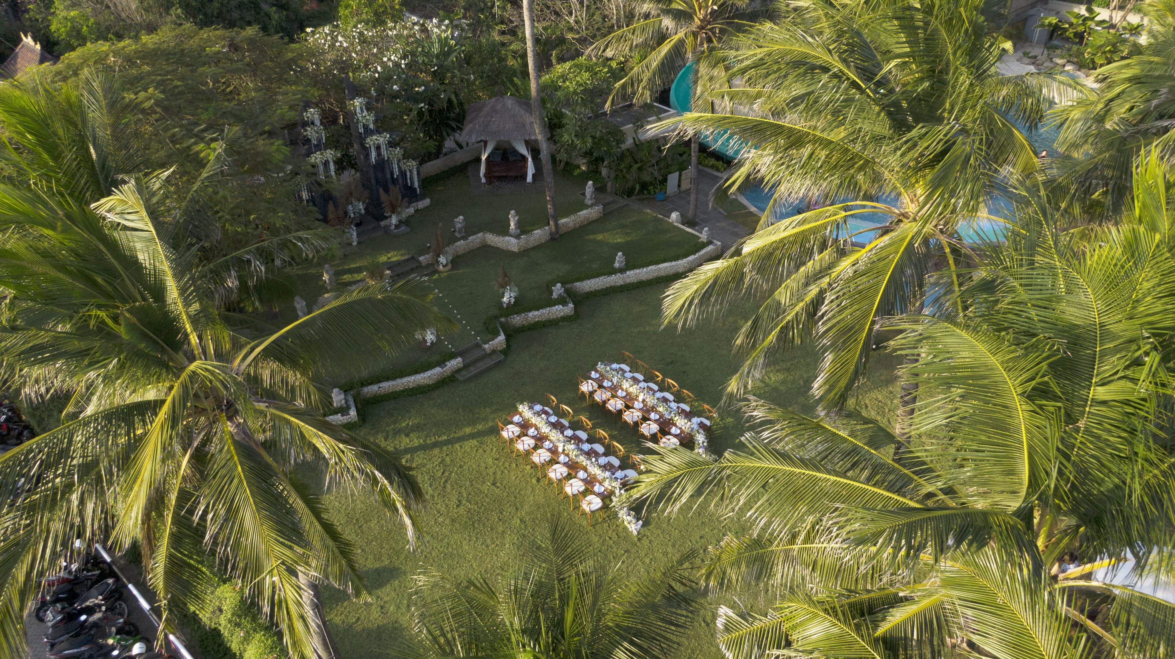 Ein Luftbild eines tropischen Resorts mit einem im Freien gelegenen Essbereich, umgeben von Palmen und einem Swimmingpool.