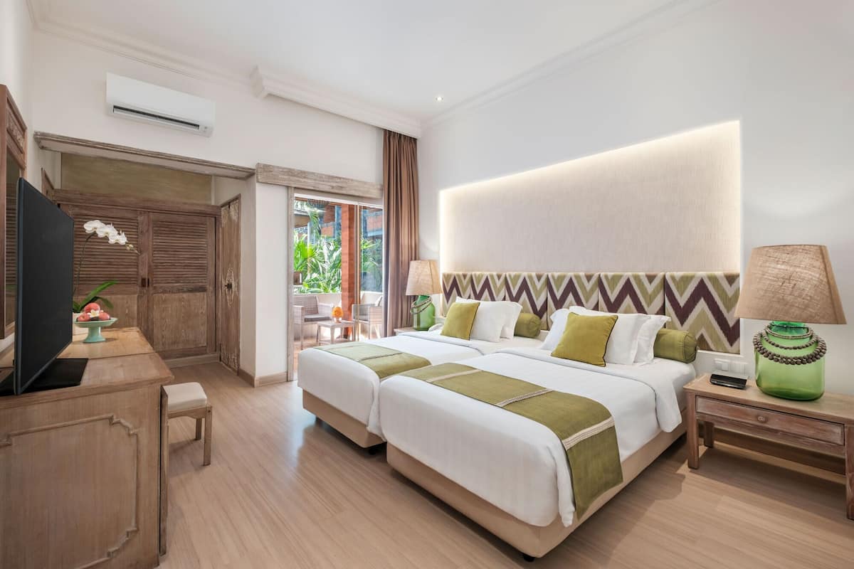 A hotel room with two beds, a desk, a TV, and a view of the outdoors.