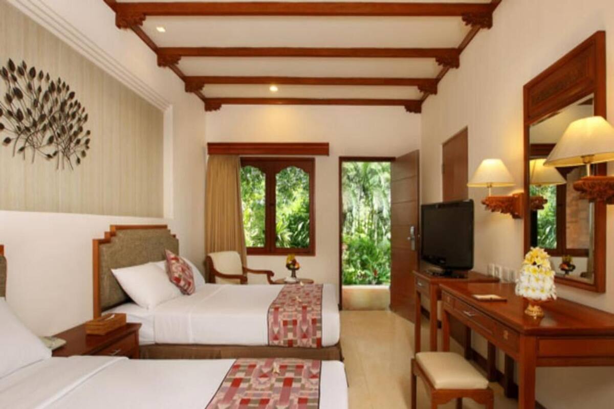 A hotel room with a bed, a desk, a television, and a window with a view of greenery.