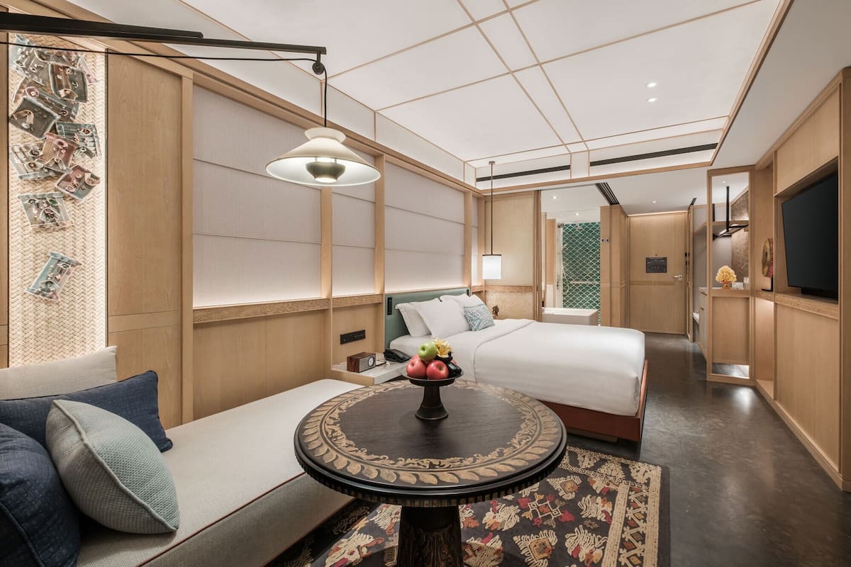 A hotel room with a sofa, two beds, a round table, and a television.