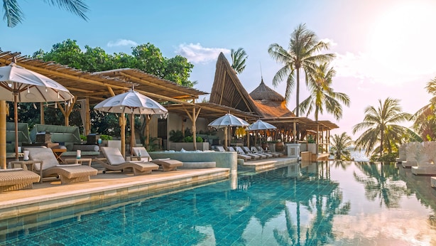 A poolside area with lounge chairs and umbrellas, surrounded by palm trees and a clear sky. - Bali Mandira Beach Resort & Spa (Legian)