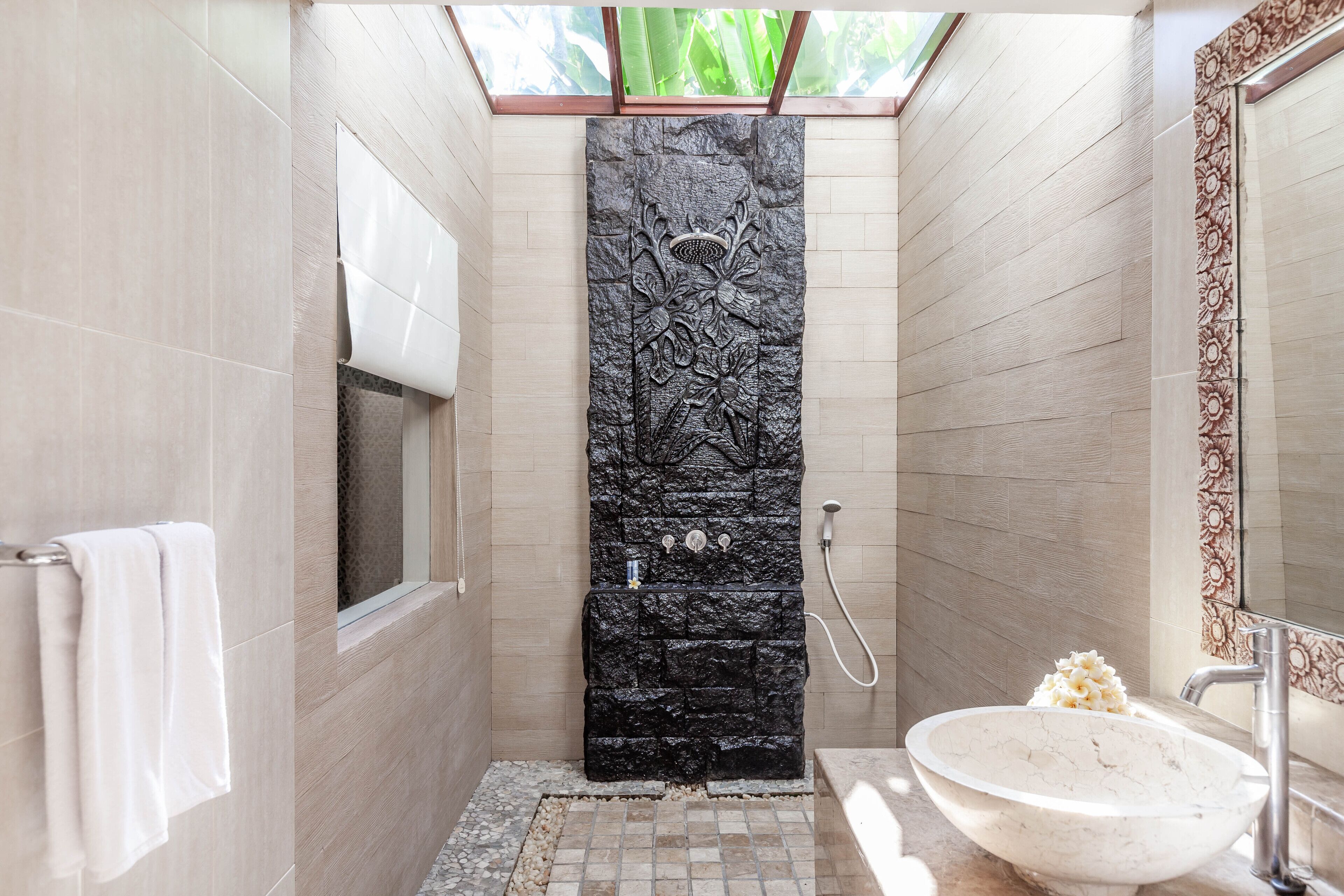 A modern bathroom with a stone wall, a white sink, and a window above the shower.