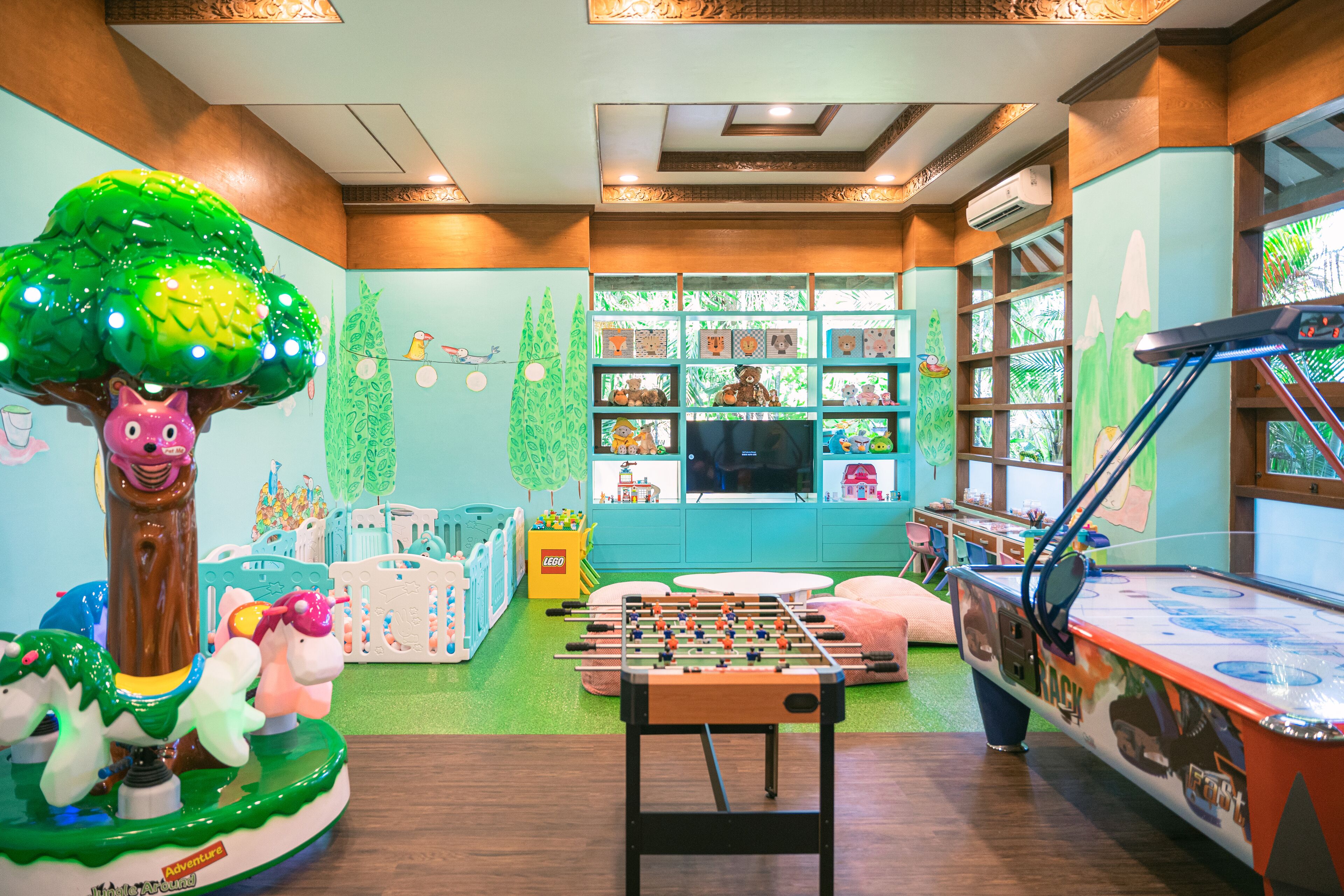 A children's playroom with a foosball table, a large tree decoration, and shelves with toys and books.