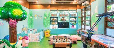 A children's playroom with a foosball table, a large tree decoration, and shelves with toys and books.