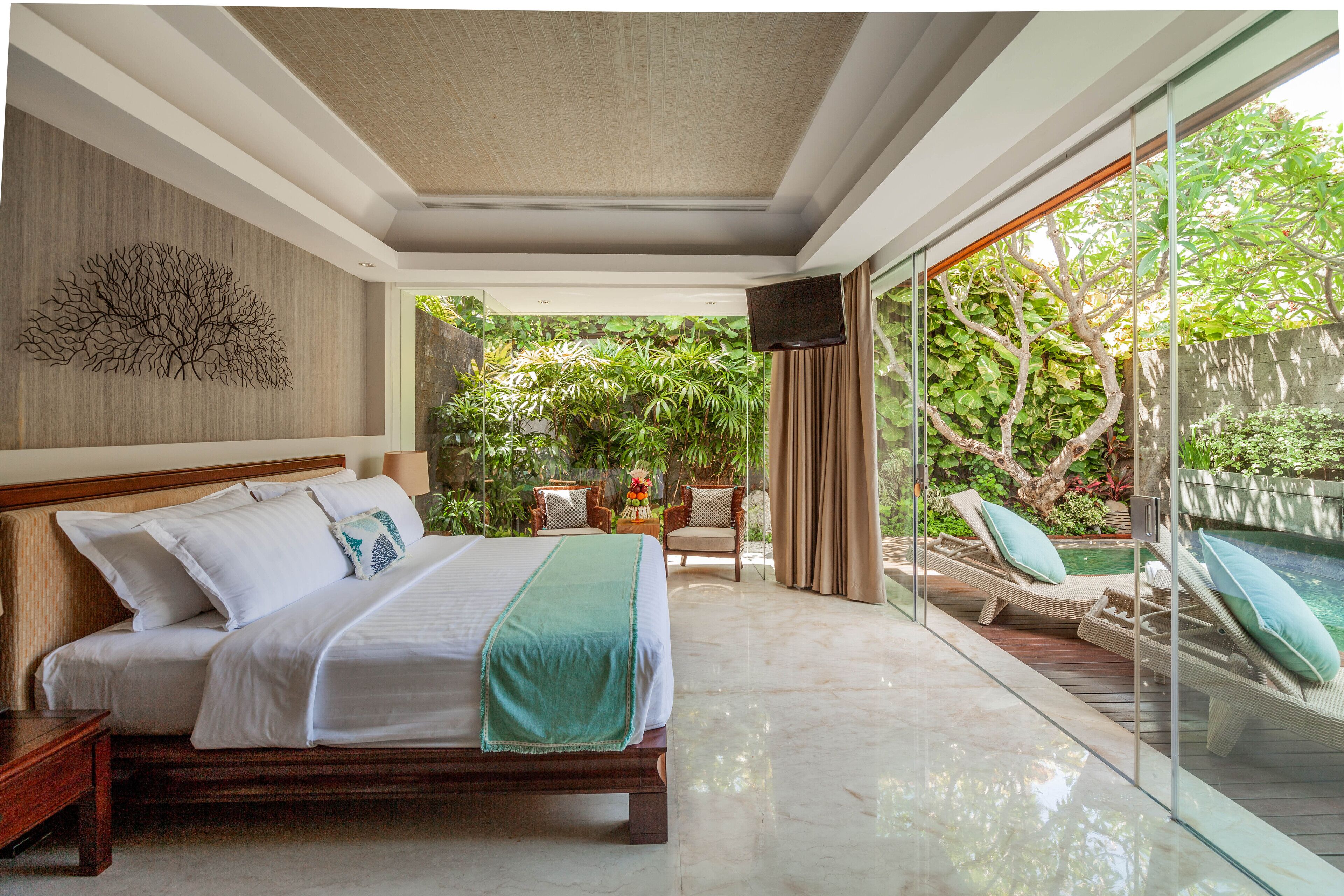 A spacious bedroom with a large bed, a wooden headboard, a wall art piece, and a view of an outdoor area with a pool and lounge chairs.