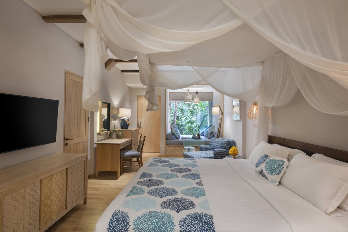 A bedroom with a bed, bedside table, TV, and a view of the outdoors.