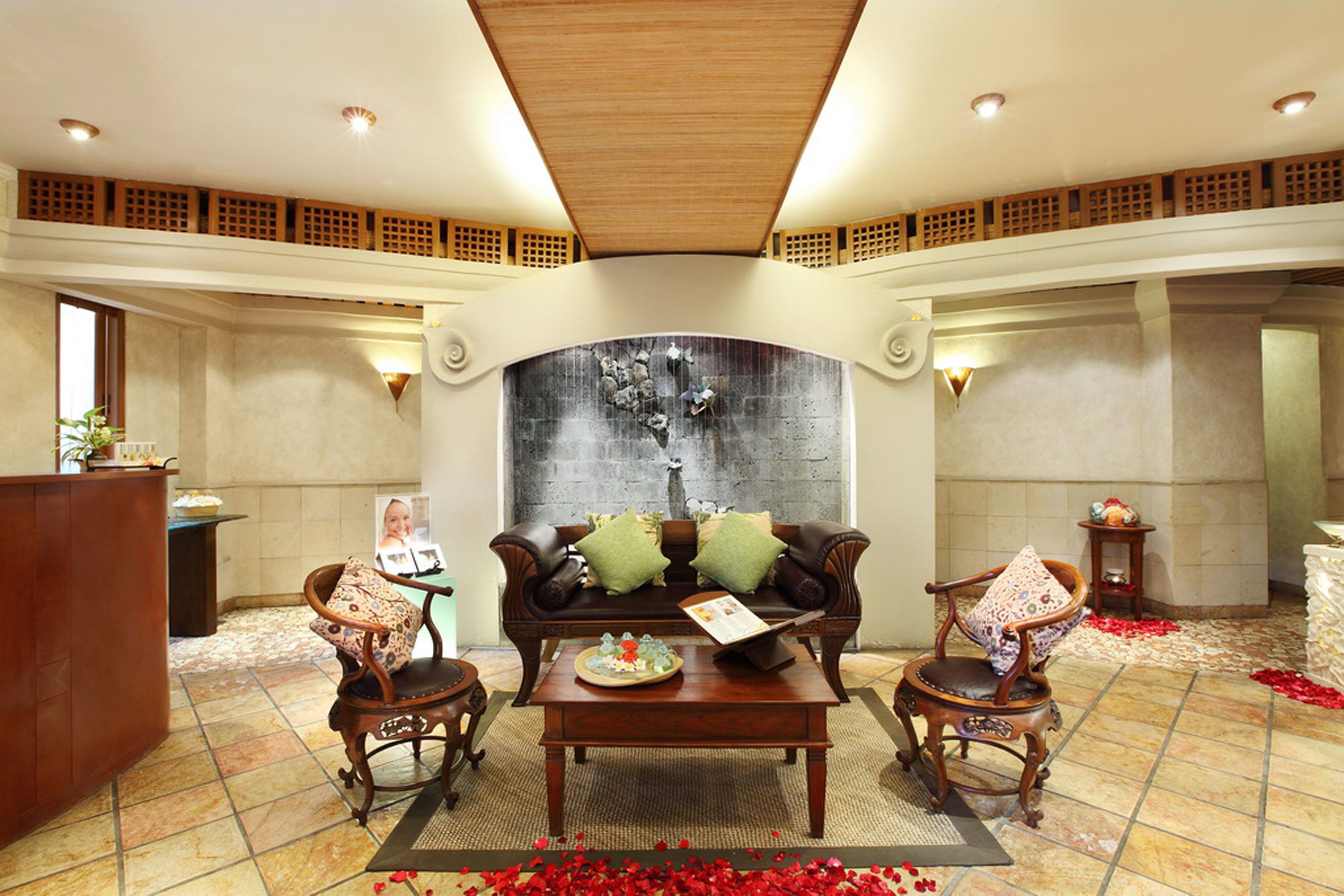 Un lobby amplio con techo alto, un área de estar central con sofá y sillones, un mostrador de recepción y una pared decorativa.