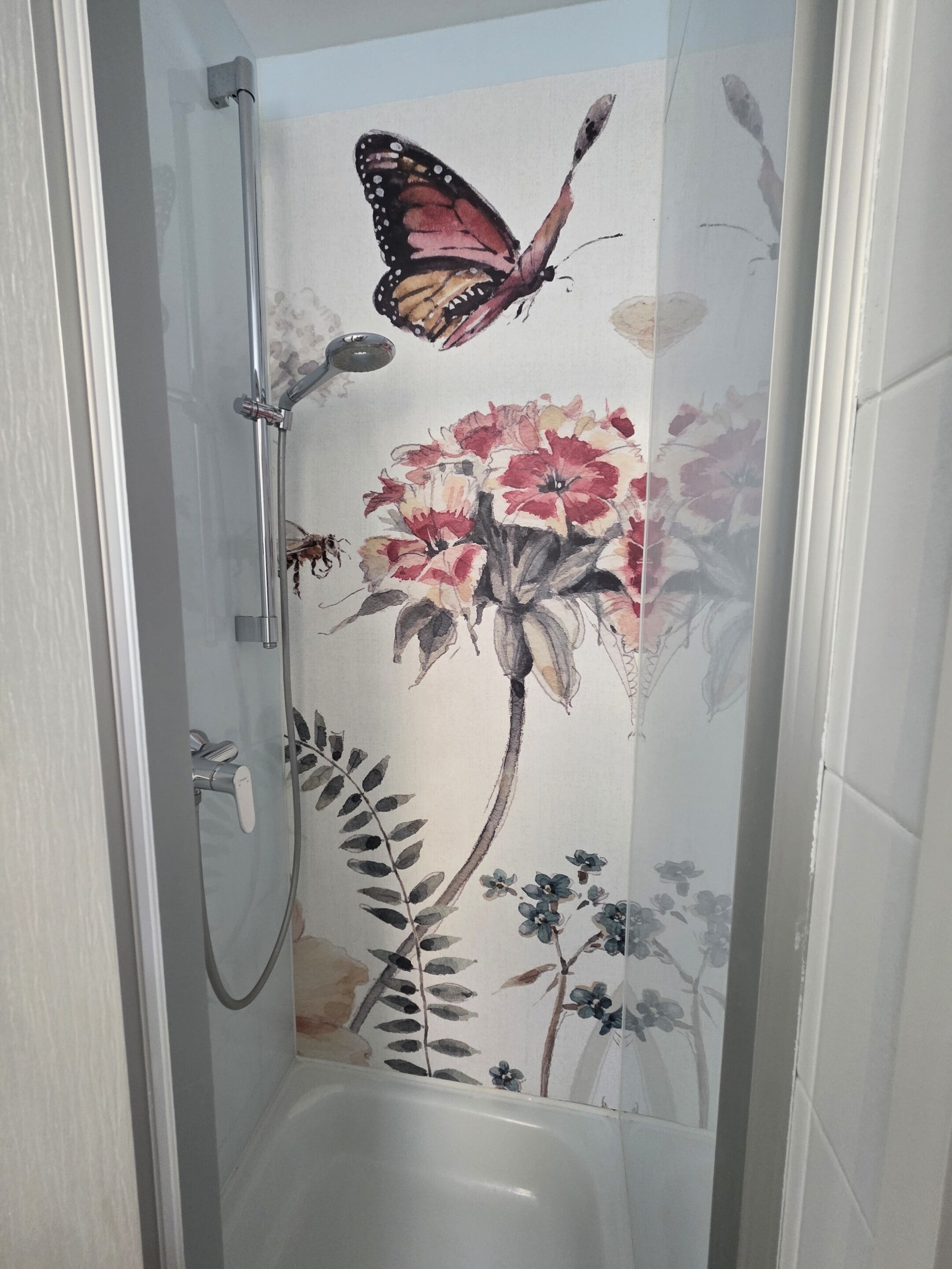 Chuveiro com mural floral e de borboletas, chuveiro manual e banheira padrão.