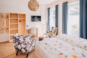 Un dormitorio con una cama de madera, dos sillones florales, un escritorio y un armario.