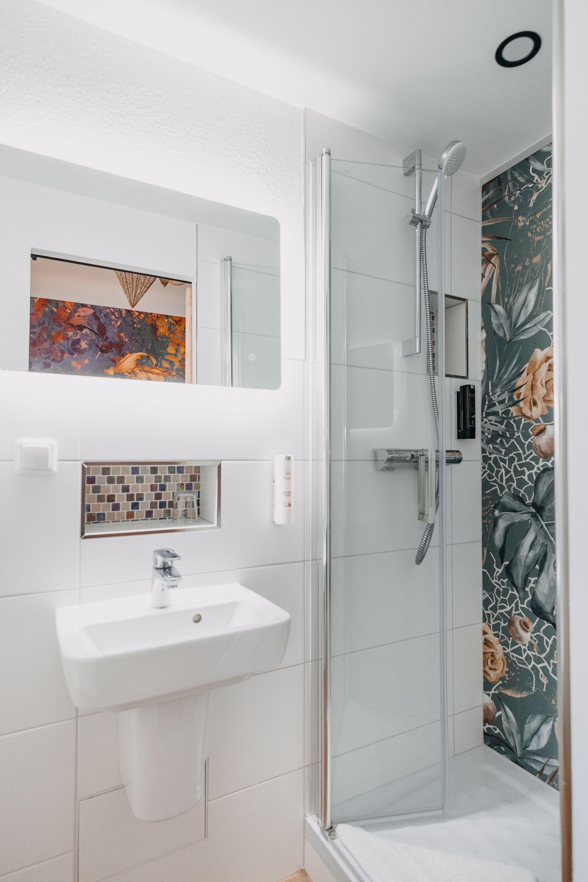 A modern bathroom with a glass-enclosed shower, a white sink, and a decorative tile backsplash.