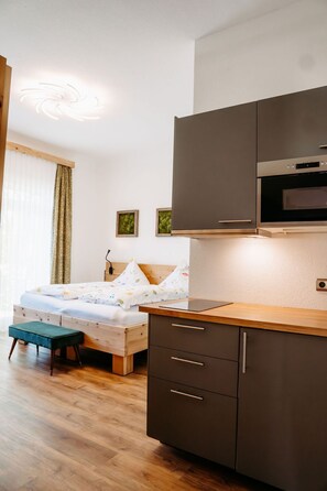 A modern bedroom with a wooden bed, a small desk, and a kitchenette with dark cabinets and a microwave. - Hotel Arabella (Bad Nauheim)