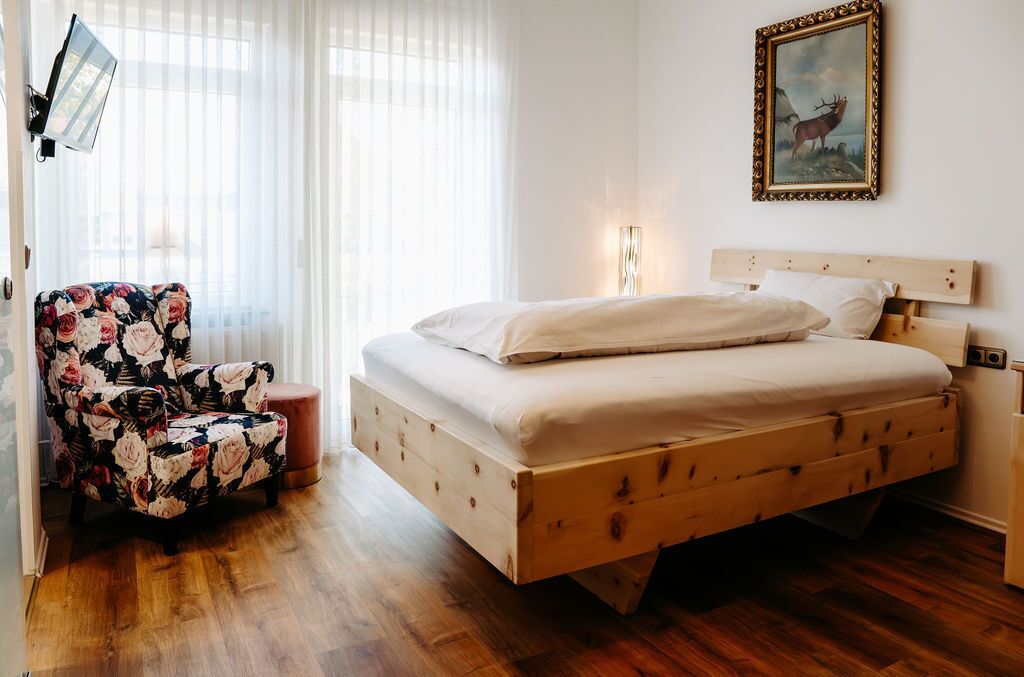Une chambre à coucher avec un lit en bois, un fauteuil à motifs floraux et un tableau accroché au mur.