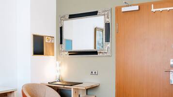 Quarto compacto com uma escrivaninha de madeira, uma cadeira vermelha, uma cama e uma porta de madeira.