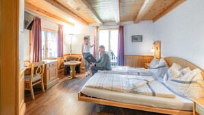 A cozy room with a wooden bed, a desk, and a chair. - Hotel Alpina (Leukerbad)